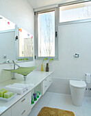 Contemporary white bathroom with large mirror and coloured glass sink and view to outside