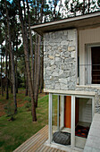 Seitenansicht eines Hauses aus Glas, Holz und Stein in einer waldreichen Umgebung