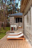 Sonnenliegen auf der Kiefernholzterrasse eines modernen Hauses aus Stein und Glas in einem Waldgebiet
