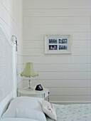 Bedside table with lamp in white painted room with photographic artwork