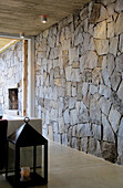 Exposed stone wall and oversized lantern in hallway with smoothed cement flooring