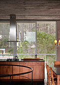 Dunstabzugshaube aus Edelstahl in einer Küche mit großen Fenstern und Einbaumöbeln aus Holz