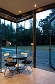 Table and chairs in corner of room with view through open glass door onto decking