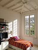 Striped bed cover on single bed in child's room with high ceiling and fan