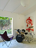 Schlagzeug und Klappstuhl im Spielzimmer mit großem Fenster und an der Wand befestigten Kunstwerken
