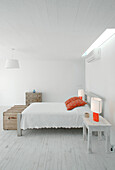 White pique bedspread with red Kilim cushions in bedroom with travelling trunk and hanging lamp made of grosgrain ribbons