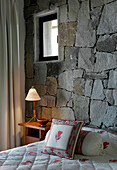 Matching bed linen and exposed stone wall with lit lamp on nightstand
