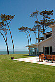 Außenansicht eines Strandhauses in einem Garten mit Rasen und Bäumen und Blick aufs Meer