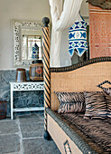 Cane bed with animal print upholstery in bedroom with exposed stone floor