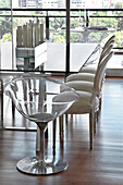 Glass topped dining table with reflective light and chairs on wooden floor