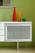 Sideboard unit with coloured glassware set against green wall