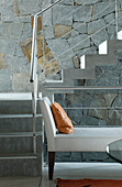 Leather day bed below concrete stairs set against exposed stone wall