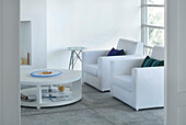 White living room with cushioned armchairs and circular coffee table
