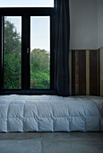 Duvet on low bed below window with view to garden
