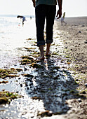 Rückansicht eines Mannes, der barfuß am Strand entlang läuft