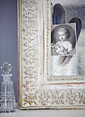 Corner of carved picture frame with glass decanter and black and white portrait picture