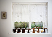 Carved wooden ornaments on sunlit window with lace curtains