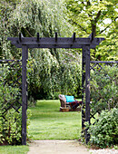 Blick durch einen hölzernen Torbogen auf einen Sitzplatz im Garten mit Rasen