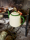 Cream teapot with green trim on fireplace stove