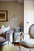 Living room with Louis XV armchair and mirrored chest of drawers with family portraits and desk lamp beside sofa