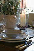 Weißes Porzellan und brennende Kerze auf dem Esstisch mit floralem Tafelaufsatz