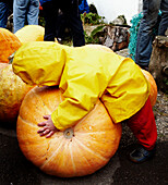 Child in raincoat holding pumpkin at summer fete