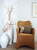 Cane armchair with cushions and twig arrangements in vases