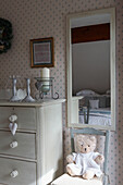 Painted chest of drawers next to mirror with teddy bear on chair