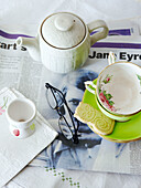 Teekanne und Teetasse mit Brille auf Zeitung