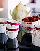 Hübsche rosa und weiße Porzellantassen und -schalen mit Erdbeeren auf einem Tisch