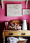 Gestrickte Teekuchen und Teekesselchen auf einer Anrichte in einem rosa Zimmer mit Kunstwerken