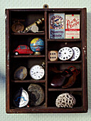 Holzkiste mit Fächern, in denen alte Erinnerungsstücke wie Uhren, Fossilien und Zigarettenschachteln ausgestellt sind