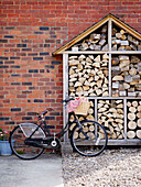 Fahrrad geparkt mit geschnittenem Brennholz an einer Backsteinfassade