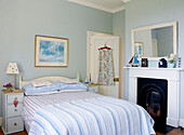 Sommerkleid hängt an der Rückseite der Tür in einem frischen blauen Schlafzimmer mit originalem Kamin
