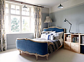 Blue and head and footboards on bed at window with wooden bedside storage unit