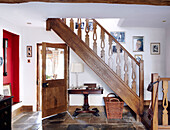 Family photographs hang on staircase with wooden banister in flagstone entrance foyer