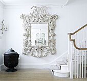 Decorative mirror in staircase with black urn and leaf scrolled frame London home UK