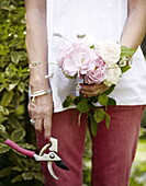 Woman stands in London garden holding cut flowers and secateurs UK