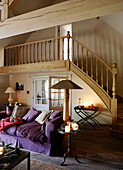 Violettes Sofa und brennende Kerzen im offenen Wohnzimmer mit Holztreppe in einem festlichen Haus in Oxfordshire, England, UK