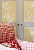 Red checked armchair with covered cupboard n bedroom of Oxfordshire farmhouse, England, UK