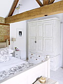 Weiß gestrichener Kleiderschrank und Doppelbett in einer umgebauten Holzscheune mit freiliegender Ziegelwand, Oxfordshire, England, UK