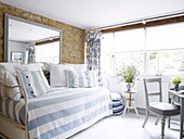 Gestreifter hellblauer Bezug auf Tagesbett mit großem Spiegel in umgebauter Scheune, Oxfordshire, England, UK