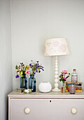 Cut flowers and lamp on painted chest of drawers in Surrey farmhouse England UK