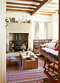 Couchtisch aus Holz auf gestreiftem Teppich mit Holzbrenner im Wohnzimmer eines Bauernhauses in Derbyshire, England, UK