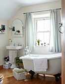 Freistehende Krallenfußbadewanne mit Sockelbecken im Badezimmer eines sonnenbeschienenen Bauernhauses in Derbyshire, Vereinigtes Königreich