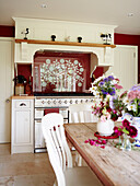 Cut flowers on wooden kitchen table with red patterned splashback in rural Oxfordshire cottage England UK