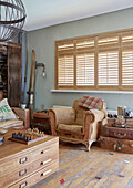 Threadbare armchair below window with Venetian blinds with vintage skis and suitcases in Sunderland home Tyne and Wear England UK