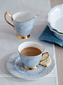 Cup and saucer with milkjug and biscuit on dining table in studio, UK