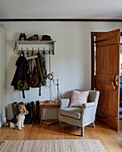 Mäntel und Taschen hängen über einem Sessel, davor Hund in einem Haus in Kent, England, UK