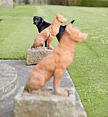 Schwarzer Labrador mit zwei Hundestatuen auf dem Gelände von Capheaton Hall in Northumberland, UK